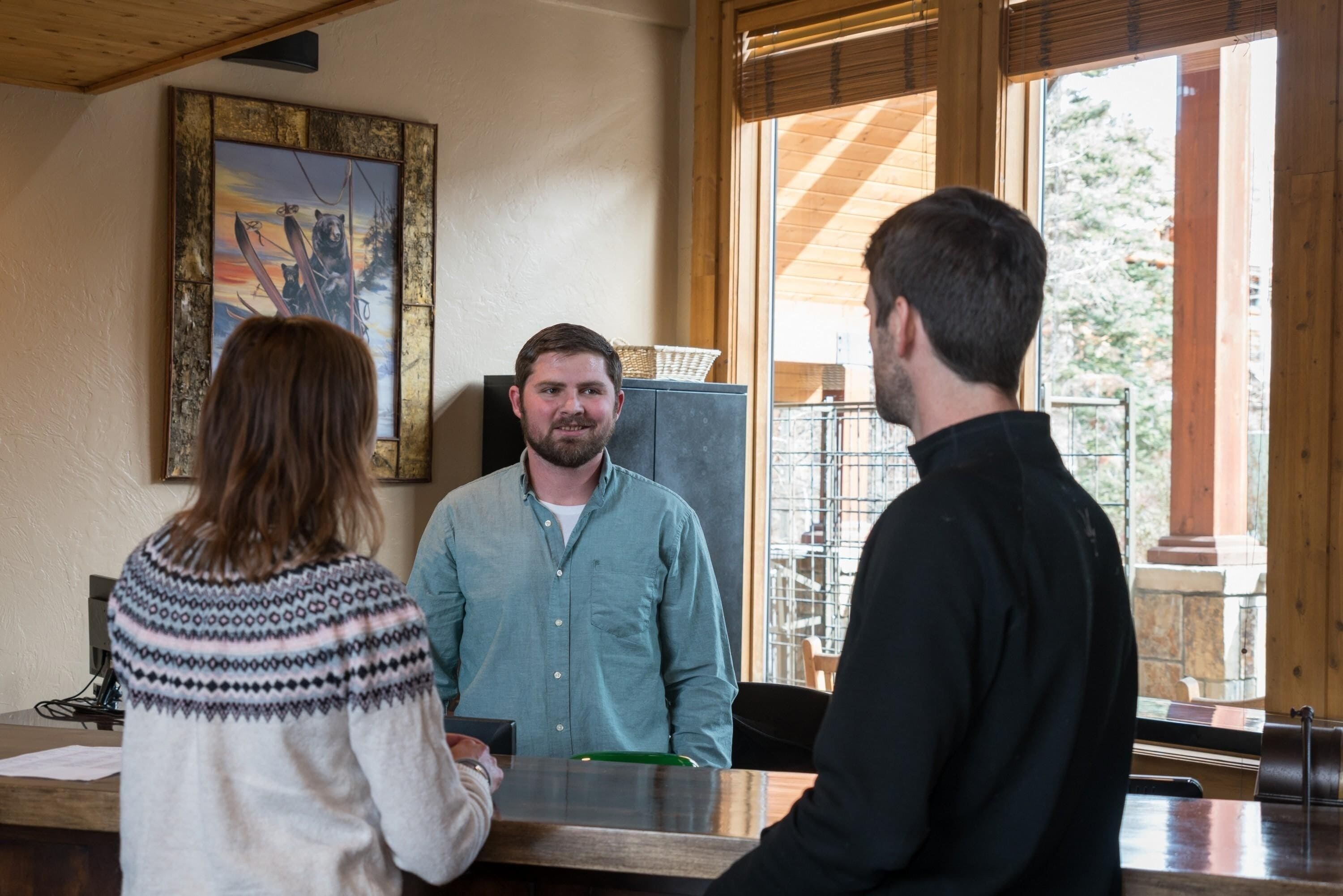 A reception area with a wooden interior, a painting on the wall, and a view of the outdoors through large windows.