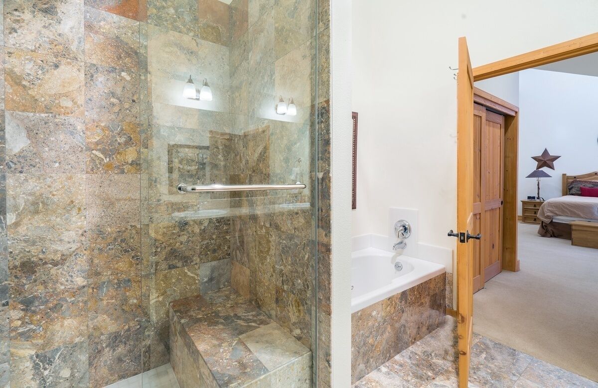 A bathroom with a glass-enclosed shower, a white sink, and a wooden door leading to a bedroom.