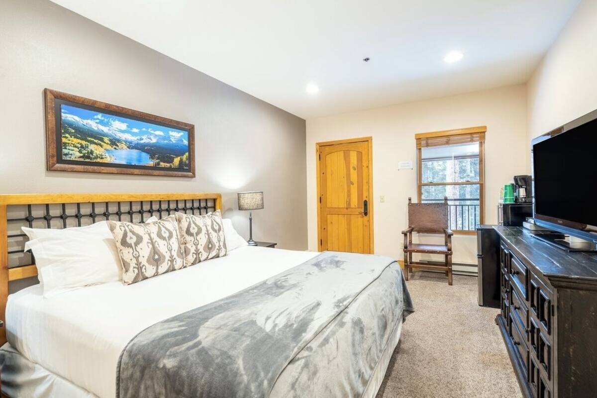 A bedroom with a large bed, a television, a wooden door, and a window.