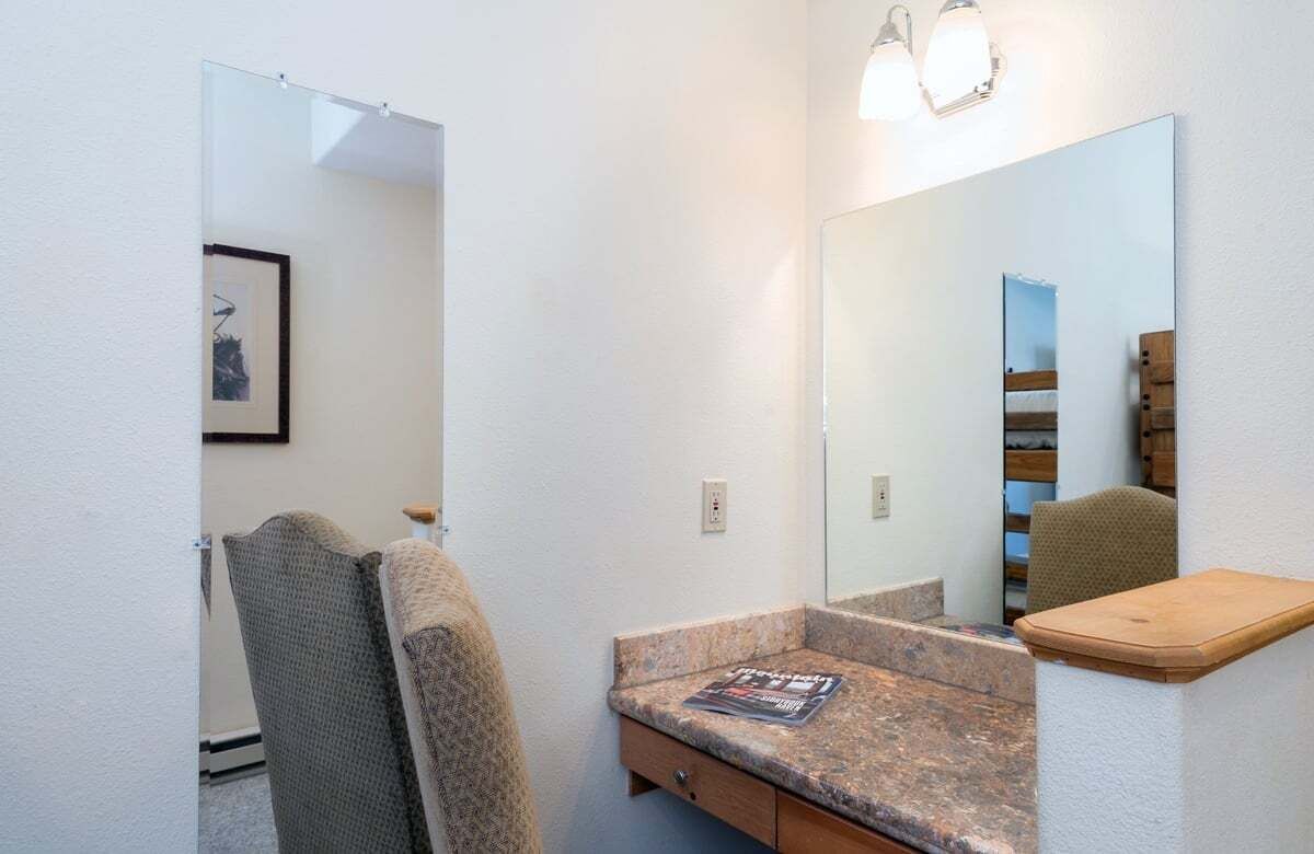 A bathroom with a large mirror, a towel rack, a sink with a magazine, and a wooden shelf.