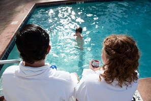 Una piscina con una persona nadando y dos personas observando desde el borde.