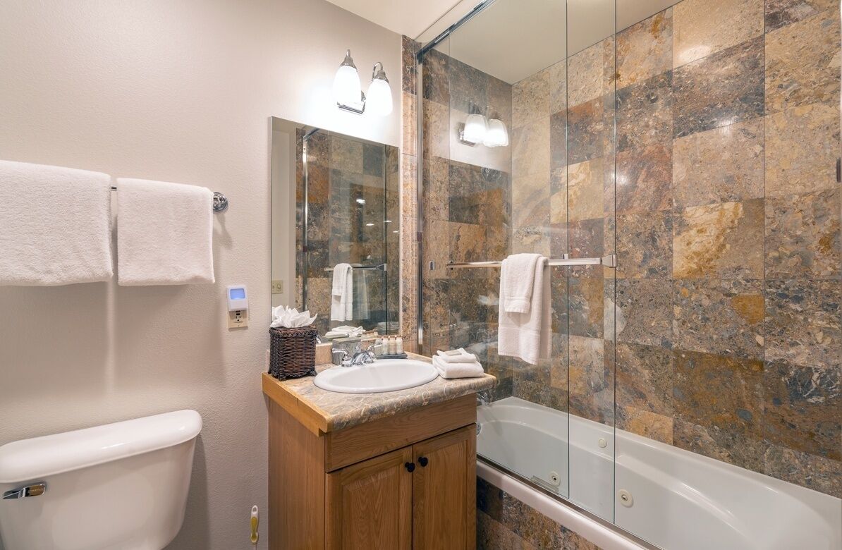 A modern bathroom with a marble shower wall, a glass-enclosed shower, a wooden vanity with a sink, and a toilet.