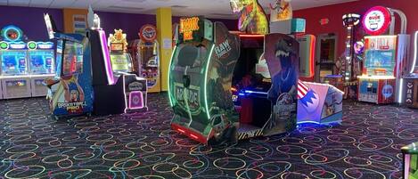 Un salón recreativo con diversas máquinas de juego, incluyendo baloncesto, carreras y un juego temático de dinosaurios.