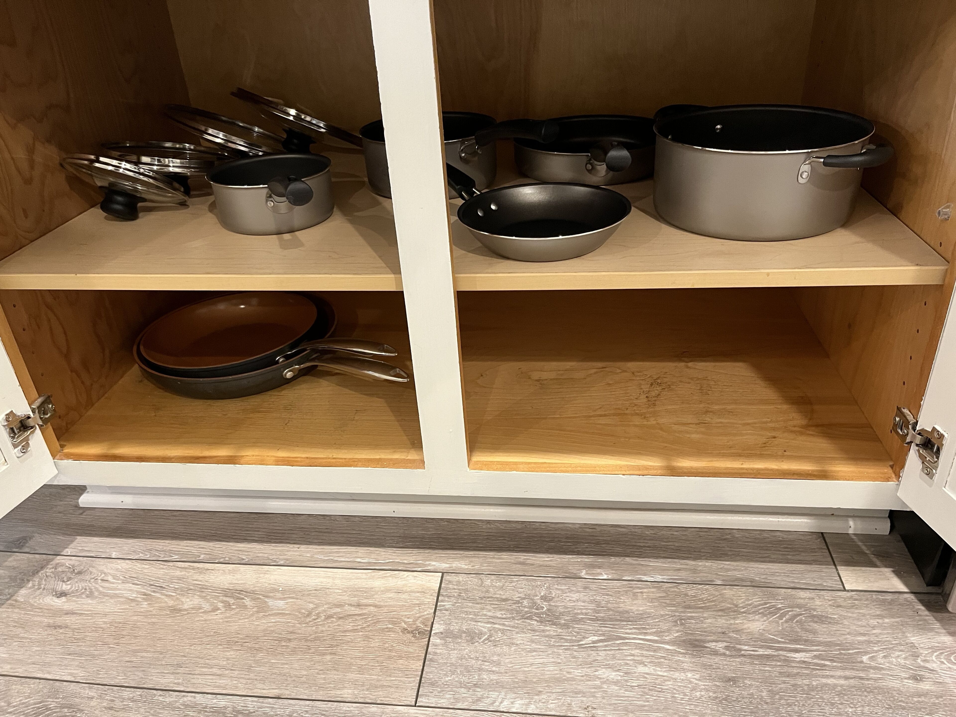 A kitchen cabinet with various cookware items including pots, pans, and lids.