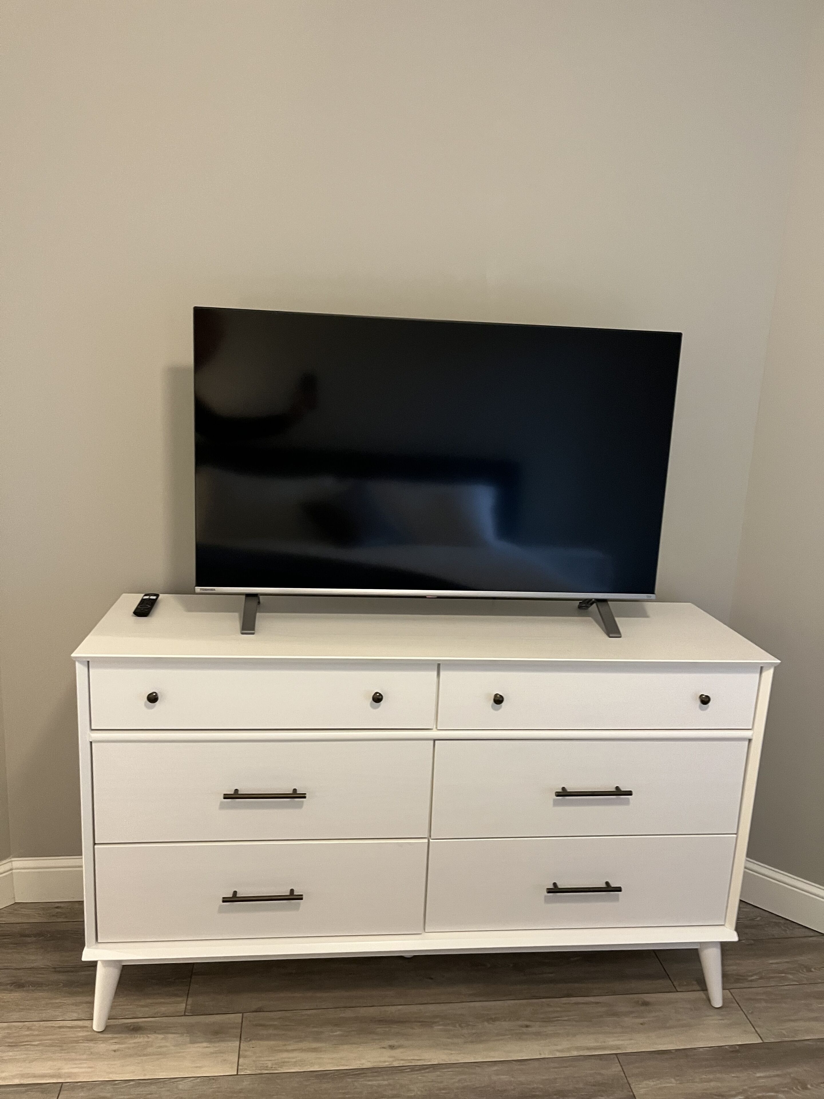 Un aparador blanco con un televisor de pantalla plana encima, cajones con pomos y un control remoto sobre el aparador.