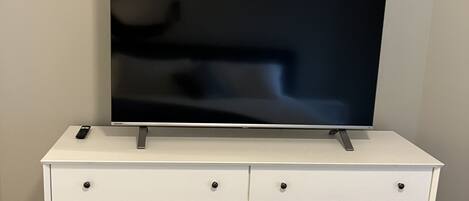 Un aparador blanco con un televisor de pantalla plana encima, cajones con pomos y un control remoto sobre el aparador.