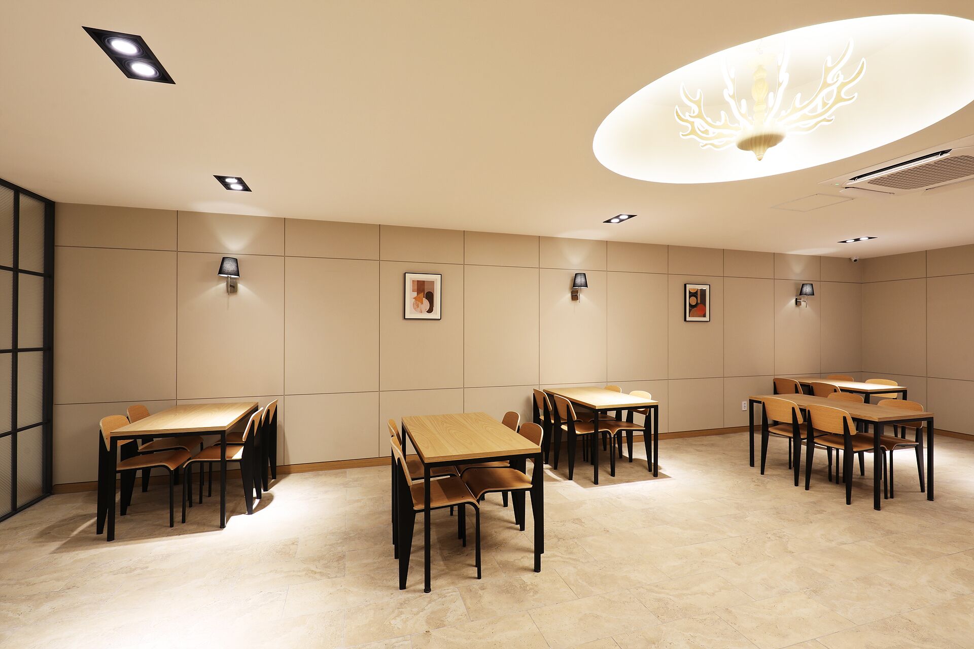 A dining area with multiple tables and chairs, recessed ceiling lights, and wall-mounted lamps.
