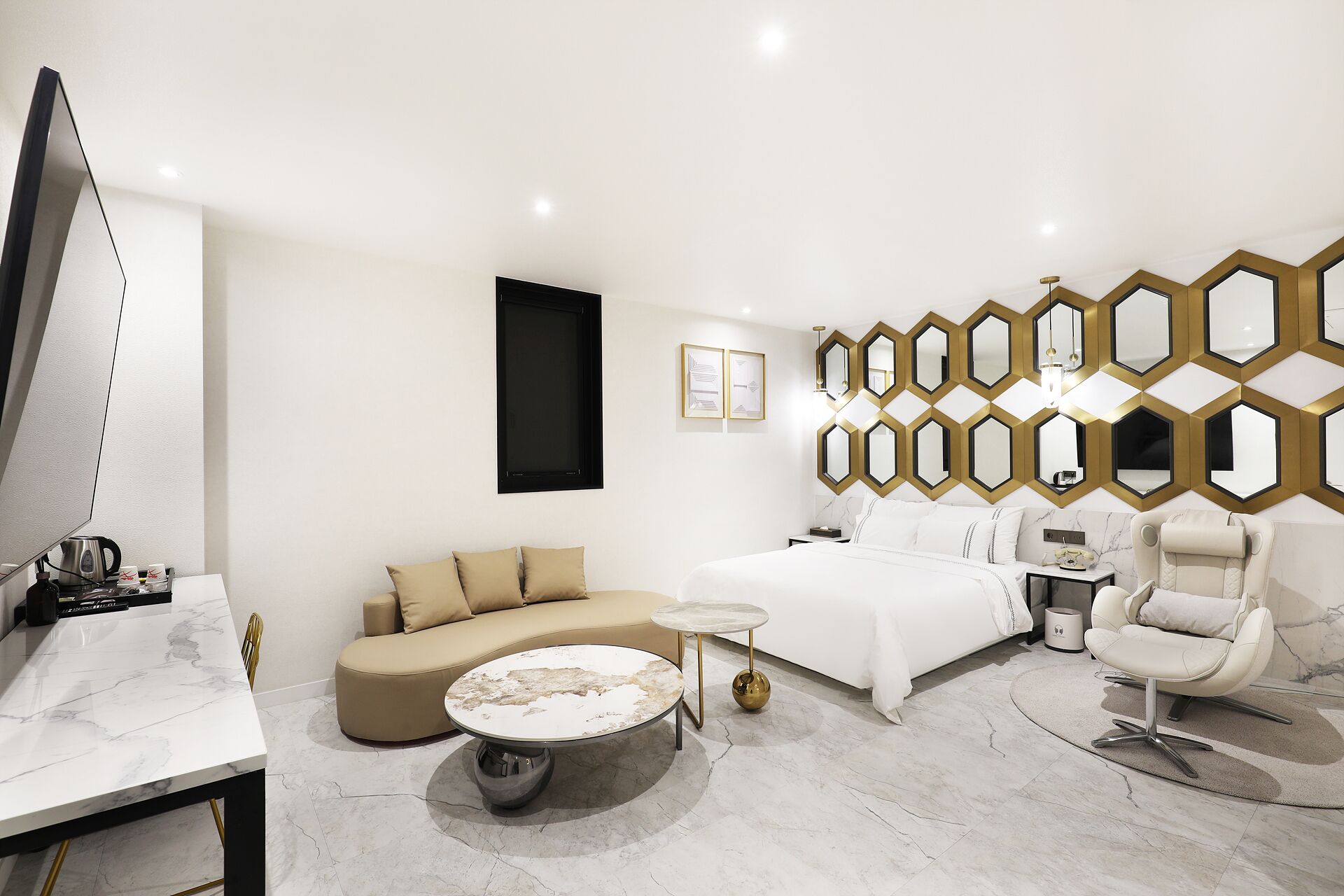 A modern hotel room with a sofa, a round coffee table, a bed, and a chair.