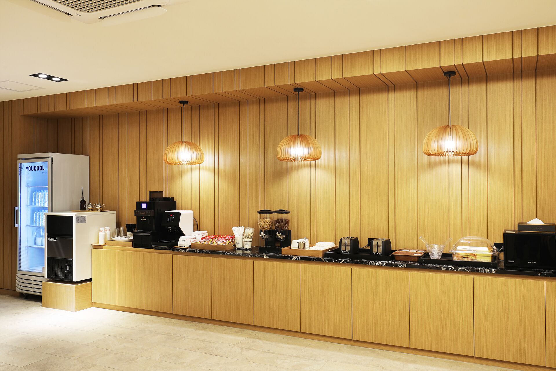 A modern kitchen with wooden paneling, a coffee machine, a refrigerator, and pendant lights.