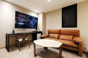 A modern living room with a large flat-screen TV mounted on the wall, a brown leather sofa, a wooden coffee table, and a wooden chair. - Mari Hotel Chungju (Chungju)