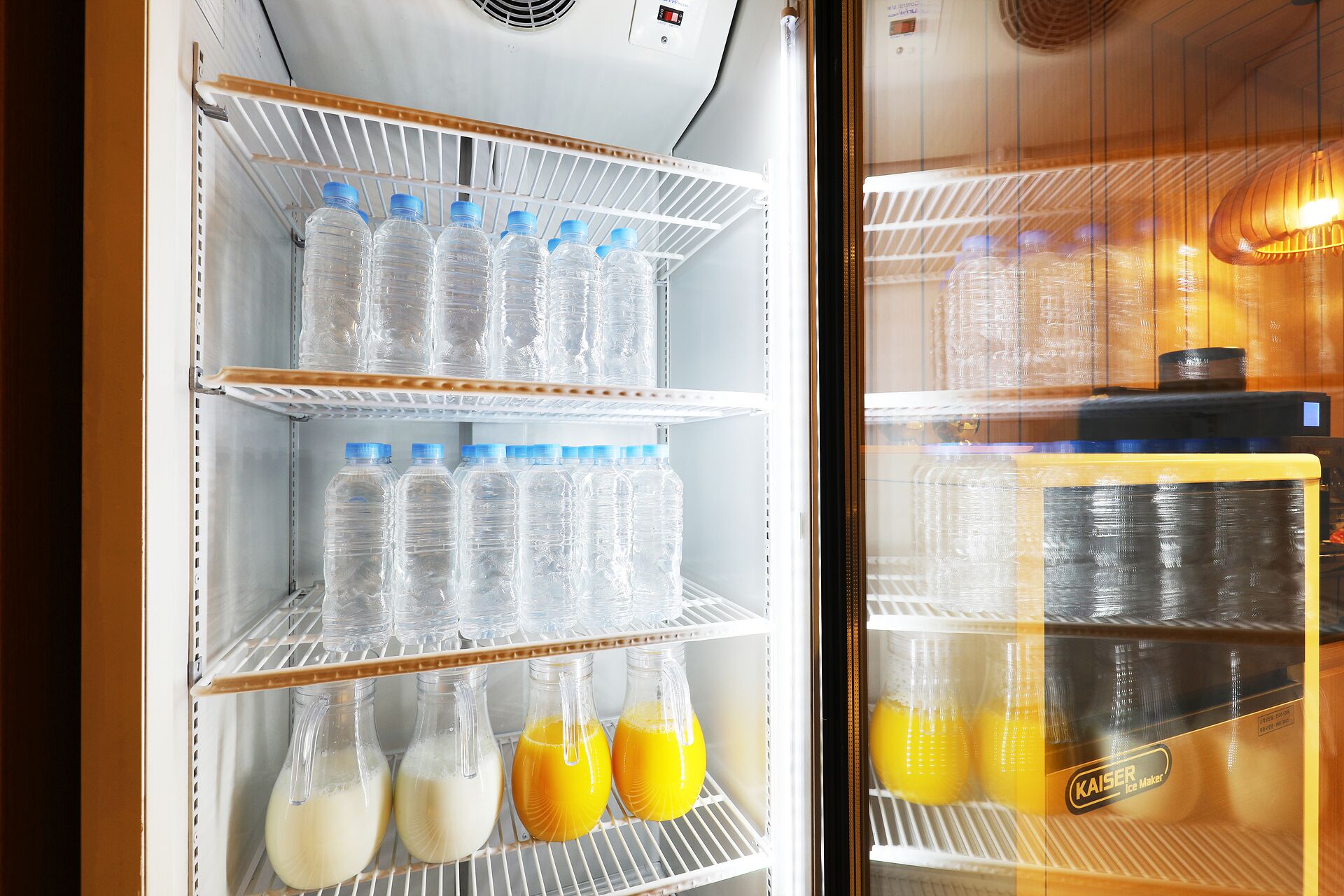 Un refrigerador con repisas que contienen botellas de plástico de agua y botellas de vidrio con leche y jugo de naranja.
