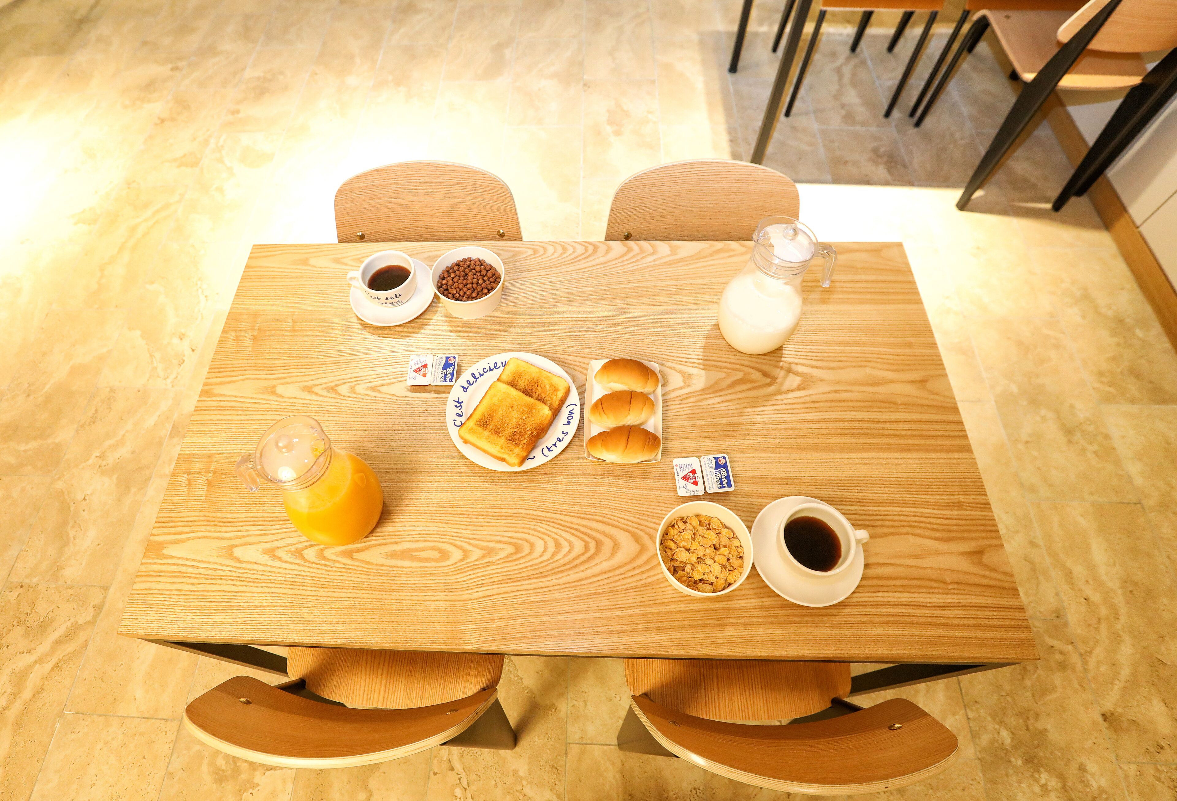 Una mesa de madera con alimentos para el desayuno, como tostadas, leche, café y cereales.