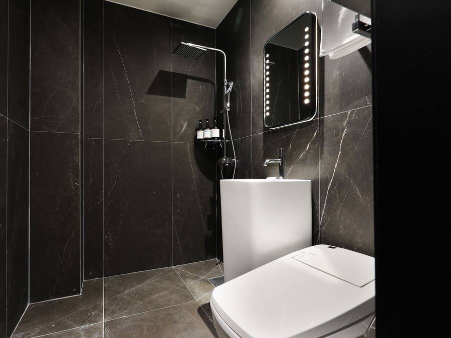 Ein modernes Badezimmer mit dunklen Marmorwänden, einem weißen Waschbecken und einer Handbrause.