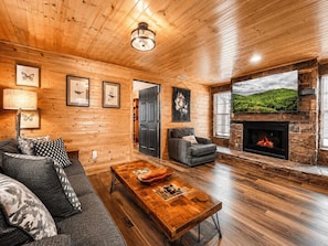 A cozy cabin interior with a fireplace, wooden walls, and a sofa. - Dolly's Castle 4 | Mountain Views | Near Dollywood | Private Balcony (Sevierville)