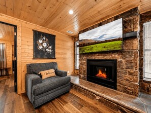 A cozy room with a fireplace, a sofa with a 'Welcome' pillow, a painting on the wall, and a scenic view on the fireplace screen. - Dolly's Castle 4 | Mountain Views | Near Dollywood | Private Balcony (Sevierville)
