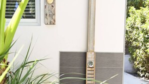 Un espace de douche extérieur moderne, doté d’un pommeau de douche en bois fixé au mur, d’un pommeau de douche à pluie en métal et d’un panneau en bois avec un thermomètre.