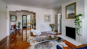 Un salon spacieux doté de planchers en bois, d’une cheminée blanche et d’un coin salon moderne.