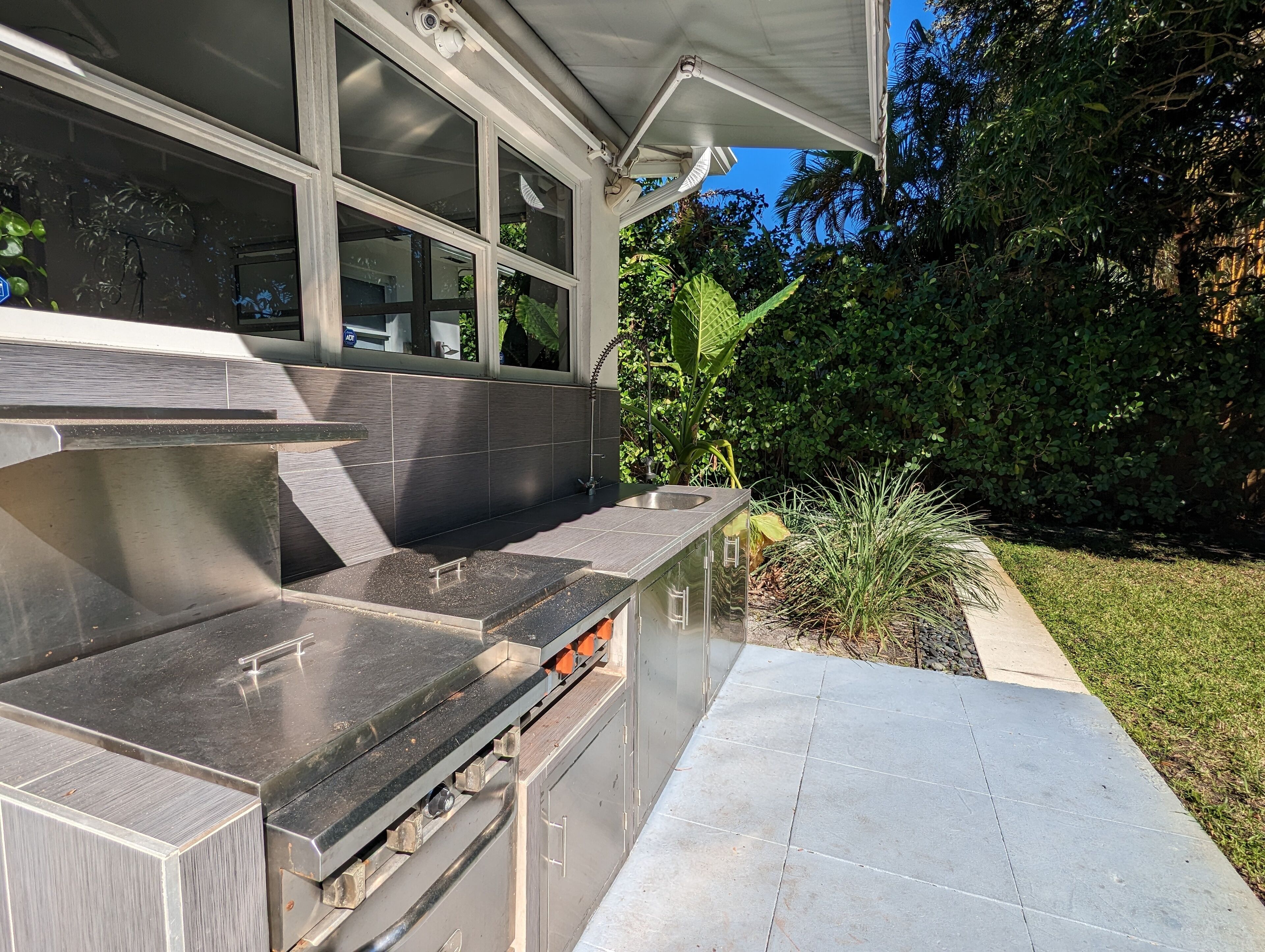 A modern outdoor kitchen with a stainless steel countertop, a sink, and a built-in oven.