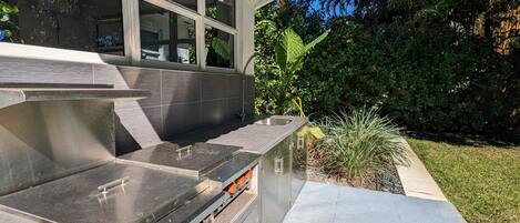 A modern outdoor kitchen with a stainless steel countertop, a sink, and a built-in oven.