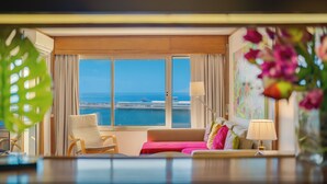 A hotel room with a large window, a sofa, a chair, a lamp, and a vase with flowers. - Apartamento Vista Pontinha (Funchal)