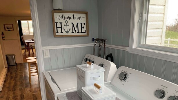 Una sala de lavandería con lavadora y secadora, un cartel que dice 'Welcome to our HOME' y una ventana con vistas.