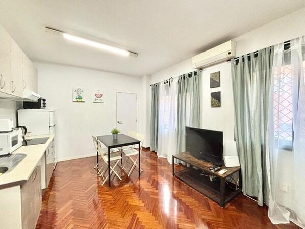 A compact living space with a kitchenette, a dining area, a TV, and a window with curtains.