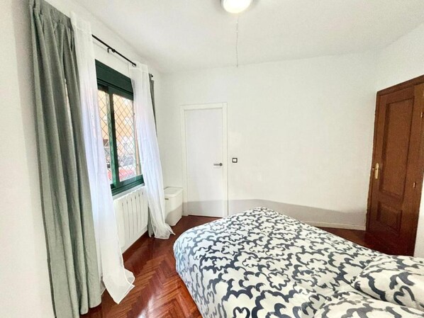 A bedroom with a bed, a window with curtains, a radiator, and a door.