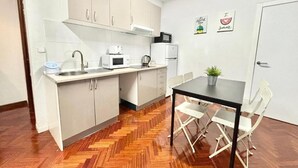 Una cocina compacta con gabinetes blancos, un microondas, una tetera y un pequeño comedor con sillas.