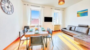 A modern living room with a dining area, a sofa, a TV, and a large clock on the wall. - Muri Di Arco (Arco)