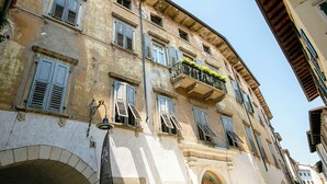 A historic building with multiple windows, some with shutters, and a balcony with plants. - Muri Di Arco (Arco)