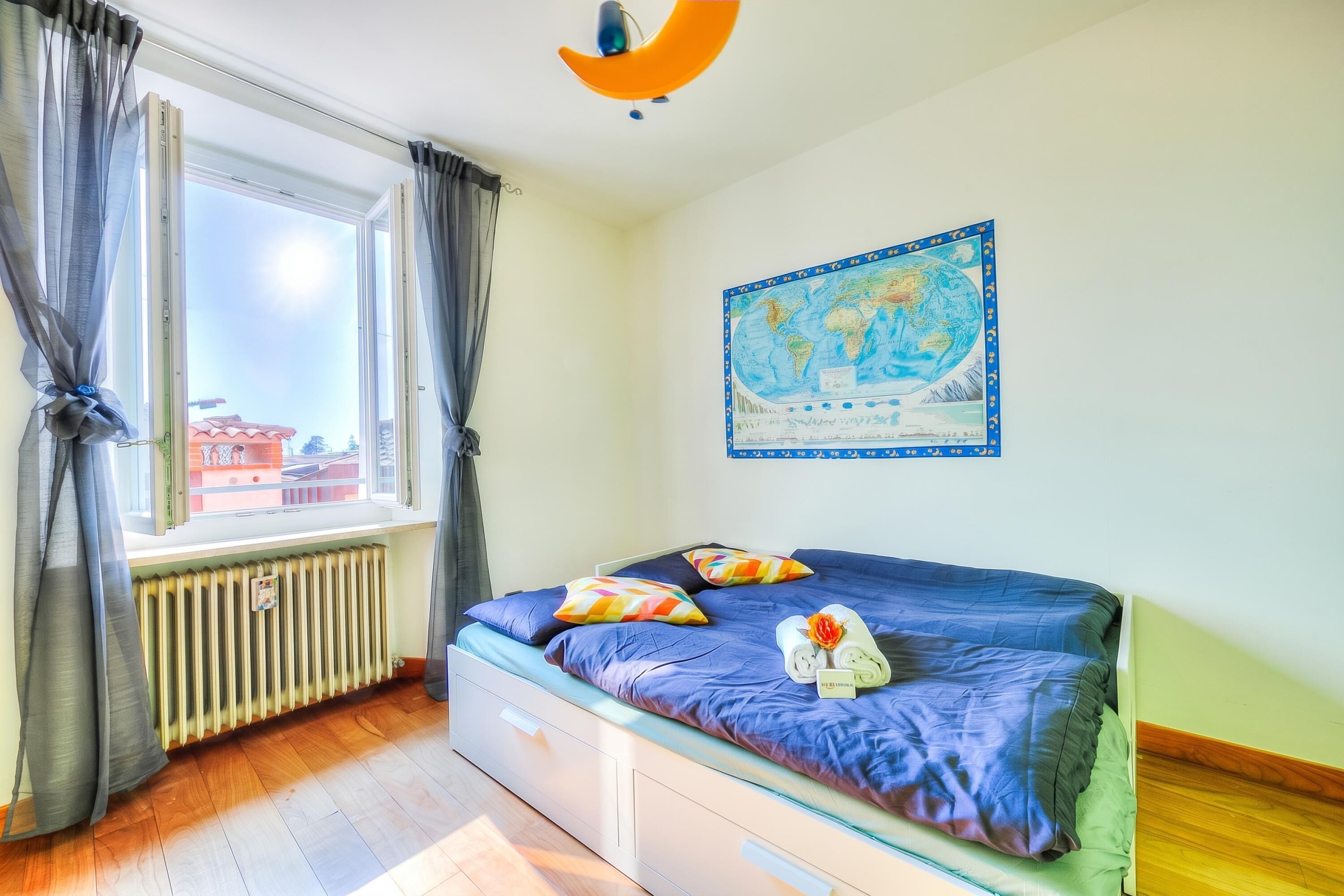 A room with a bed, a window with curtains, a radiator, and a world map on the wall.