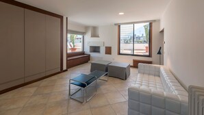 Amplia sala de estar con sofá, mesa de centro y banqueta. Grandes ventanales ofrecen vistas al exterior.