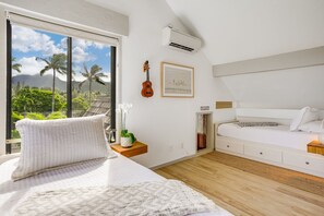 A bedroom with a bed, a guitar, a framed picture, and a view of palm trees and mountains.