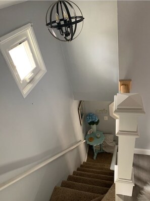 Staircase with carpeted steps and a landing, featuring a table with a vase and a lamp.