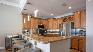 A kitchen with wooden cabinets, granite countertops, stainless steel appliances, and bar stools.