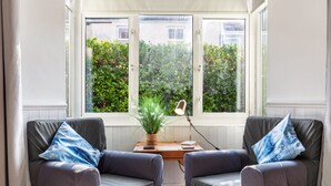 A cozy room with two grey armchairs, a small wooden table, and a potted plant. - Sunbury Villa - Close to Town and Beaches (Tenby)