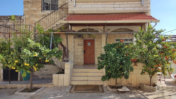 A two-story building with a red-tiled roof, a wooden door, and a small porch area.