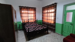 A small, simple room with a bed, a green door, and a patterned floor.