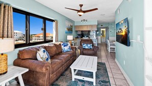 A spacious living room with a brown leather sofa, white coffee table, and a ceiling fan. - 🌞🌴Beachfront Navarre Condo | Pool + Stunning Views | Sundes 134 (Navarre Beach)