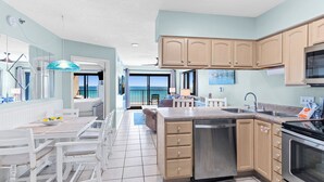 A modern kitchen with light blue walls, wooden cabinets, a stainless steel dishwasher, and a large island with a sink. - 🌞🌴Beachfront Navarre Condo | Pool + Stunning Views | Sundes 134 (Navarre Beach)