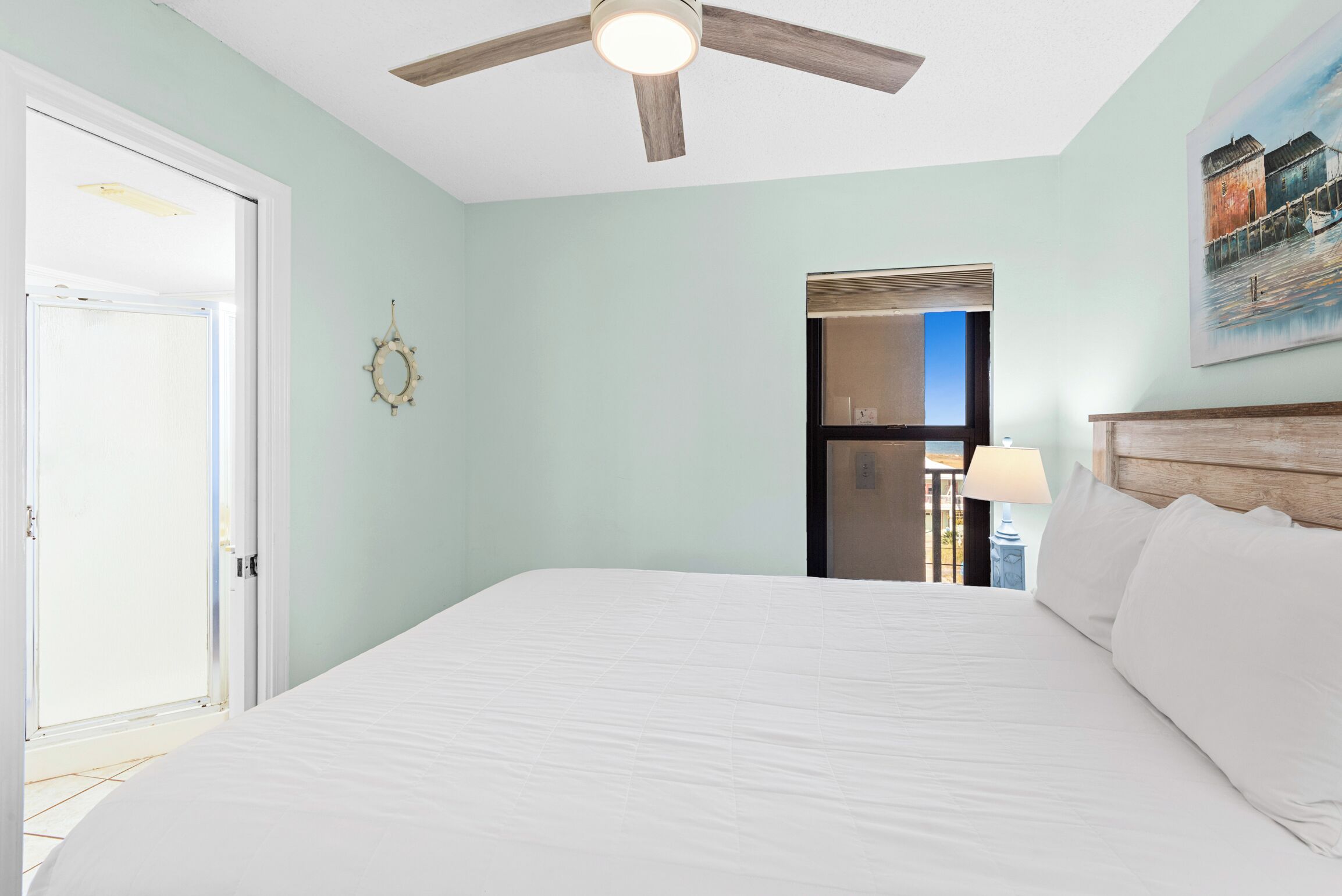 Un dormitorio con una cama, ventilador de techo, puerta, un reloj de pared y un cuadro.