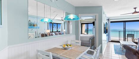 A dining area with a white table and chairs, a bowl of fruit, and a large mirror reflecting the room.