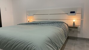 Een net opgemaakt bed met een groene sprei, twee bedlampjes en een wit hoofdeinde.