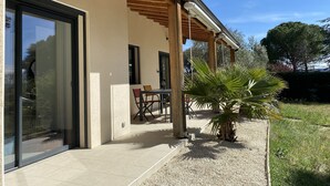 Een modern huis met een terras, een eethoek en een grote glazen deur.