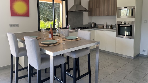 Een moderne keuken met een eethoek, met een groot schiereiland, roestvrijstalen apparatuur en uitzicht op groen.