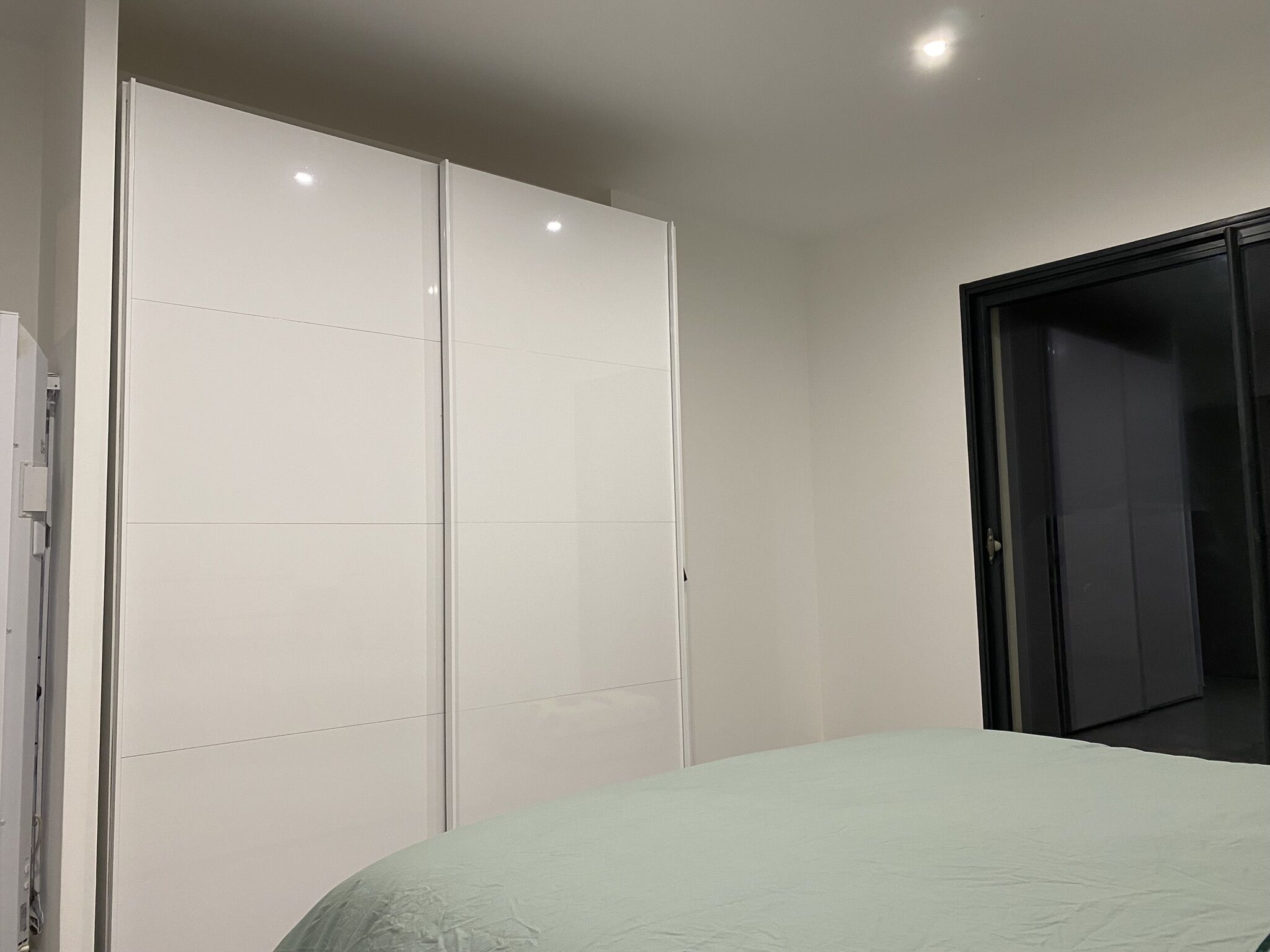 A bedroom with a bed, a white wardrobe, and a black door.