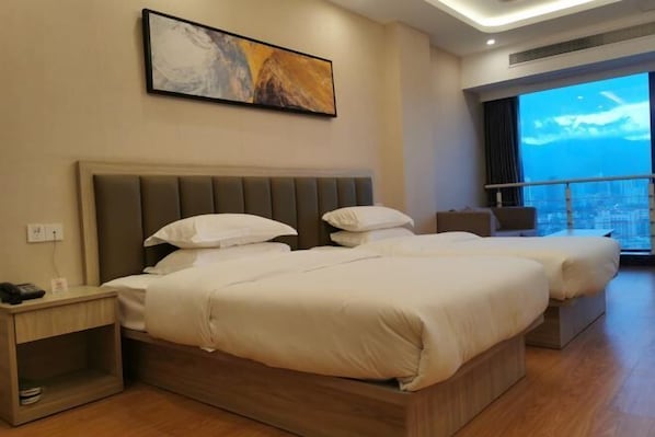 A hotel room with two beds, a nightstand, a painting on the wall, and a large window with a city view.