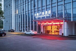 Un hôtel doté d'une façade moderne, d'une entrée imposante avec une enseigne lumineuse et d'un hall d'entrée éclairé en rouge.