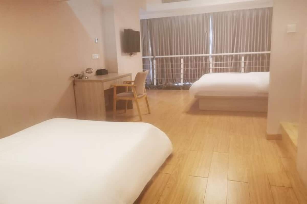 Ein Hotelzimmer mit zwei Betten, einem Schreibtisch, einem Stuhl und einem an der Wand befestigten Fernseher.