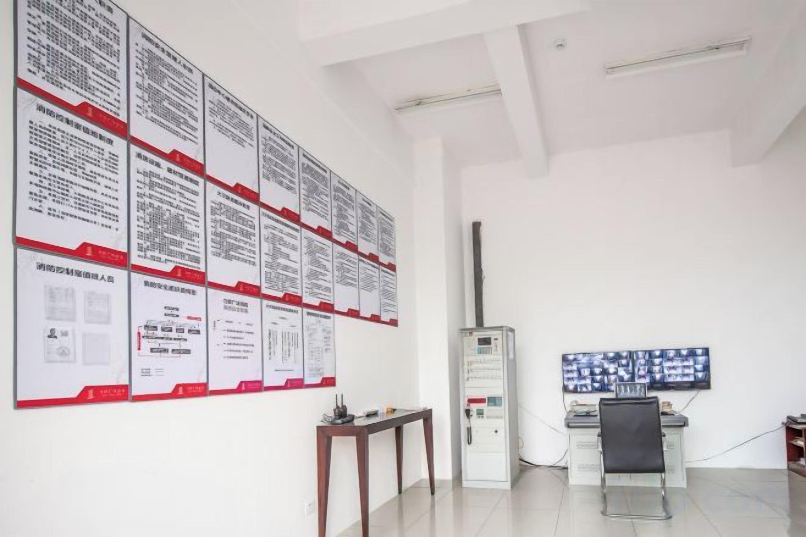 A room with a white wall displaying multiple informational posters, a desk with a computer, and a chair.